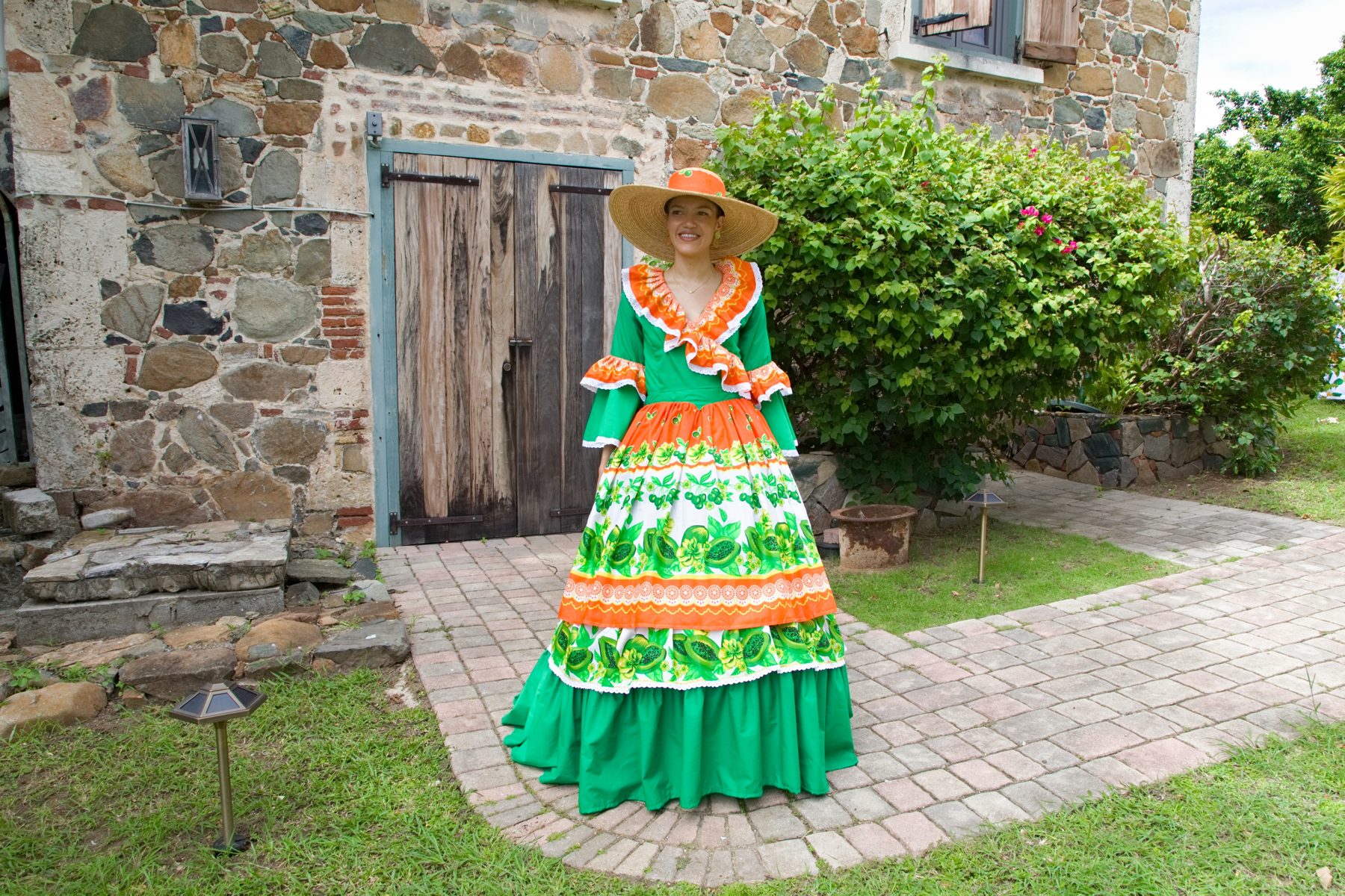 A woman in traditional dress outside a historic Sint Maarten stone building